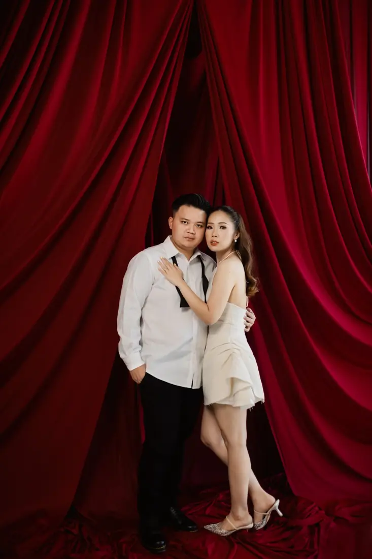 Irfan and Stephanie embracing in front of a red velvet curtain